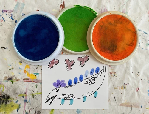 Fingerfarben in blau, grün und orange und eine Zeichnung eines Tiers, das mit Fingerfarben gemalt wurde