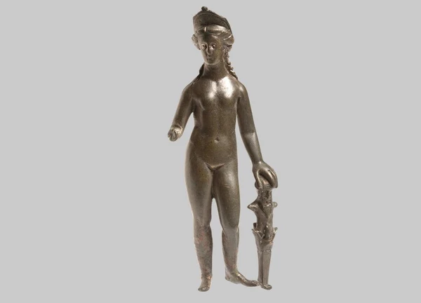 The naked standing Venus supports herself with her left hand on the ityphallic herm of the fertility god Priapus standing on the ground. Her broken-off right hand held an attribute (mirror, apple, or bowl). Her hair is tied at the nape of her neck, with individual locks falling onto her shoulder. Her head is crowned with a crescent-shaped diadem. The drilled iris contains silver inlays.