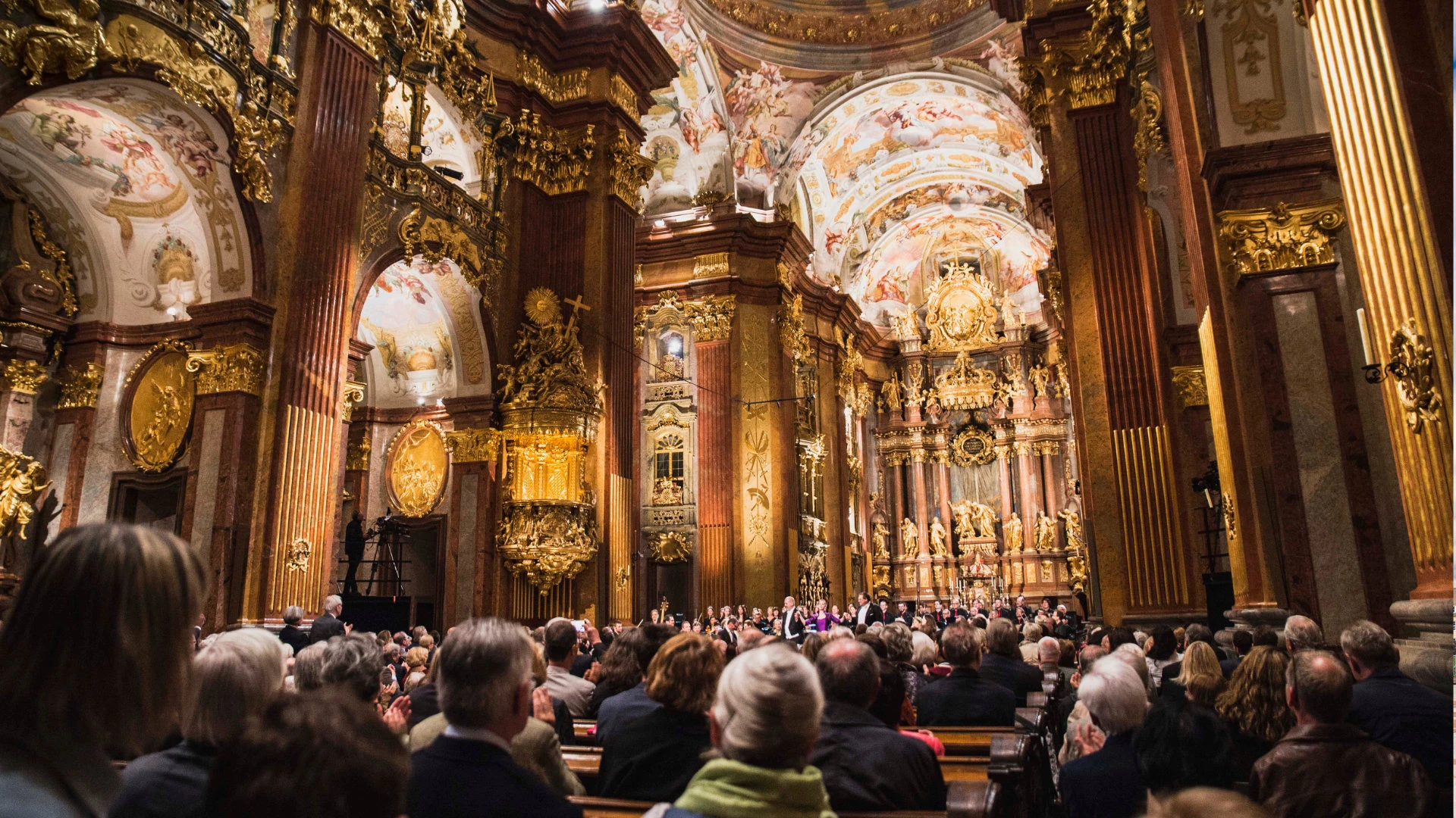 Innenansicht einer prunkvollen Barockkirche während eines Konzerts, mit üppiger Vergoldung und Deckengemälden.
