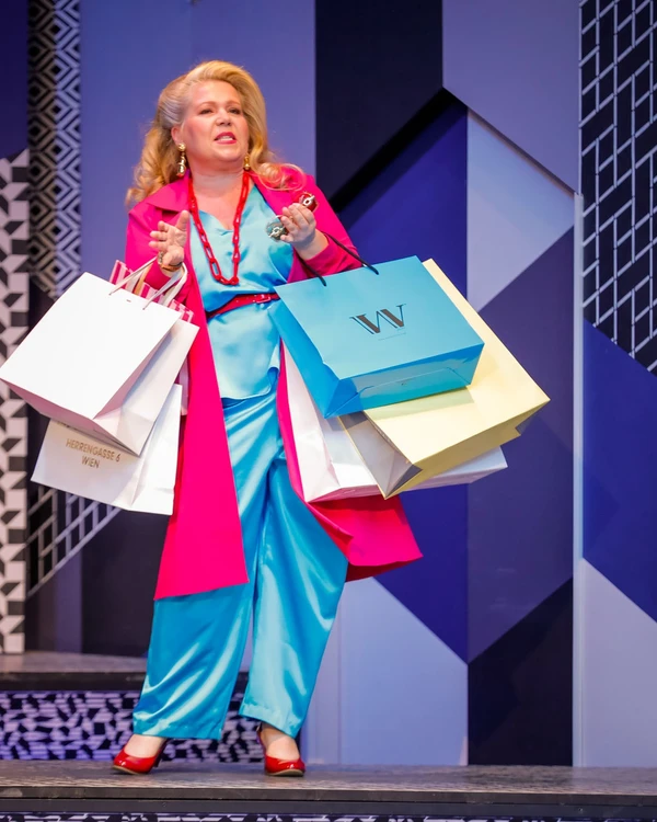 Dame mit einem blauen Kleid und pinkem Umhang hält einige Einkaufstüten in der Hand- Hintergrund ist blau mit abstrakten Muster