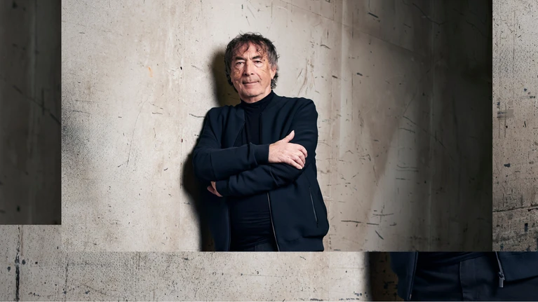 Portrait photo of Hubert von Goisern leaning against a concrete wall.