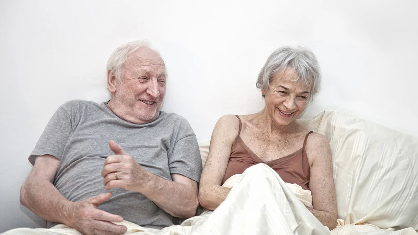 ein altes Paar im Bett in weißer Bettwäsche, sie lachen