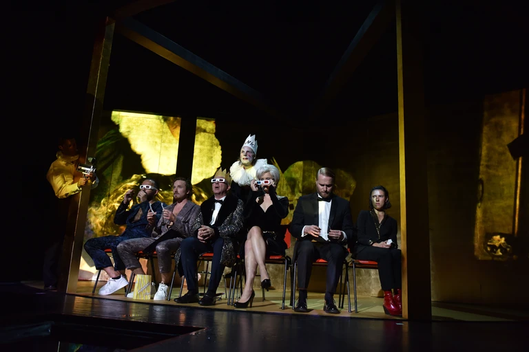 Szenenfoto aus "Hamlet". Sechs Schauspieler*innen sitzen mit dem Rücken zum König, ein paar von ihnen tragen 3D-Brillen.