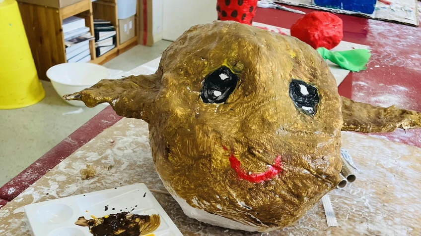 Pappeskulptur mit langen Ohren und angemalt. Vorne sind Pinsel und Farben zu sehen.