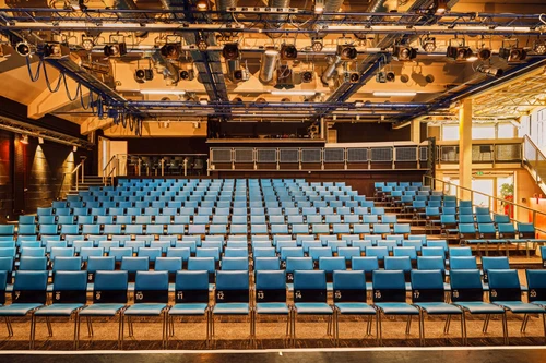 Innenansicht eines modernen Theatersaals mit nummerierten blauen Stühlen und ausgeklügelter Deckenbeleuchtung.