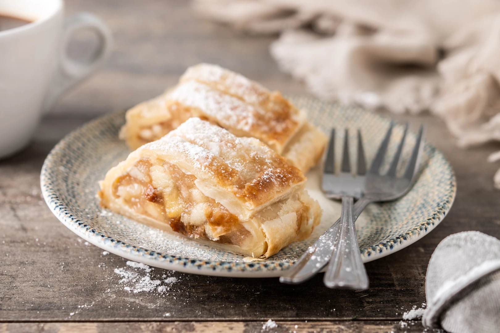 Ein angeschnittenes Apfelstrudel-Stück auf einem Teller mit zwei Gabeln. 