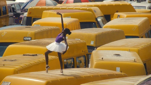 A still from the short film ‘Then Comes the Body’ by Jacob Krupnick. The image shows the roofs of several large yellow vans, with a ballerina dancing on one of them.