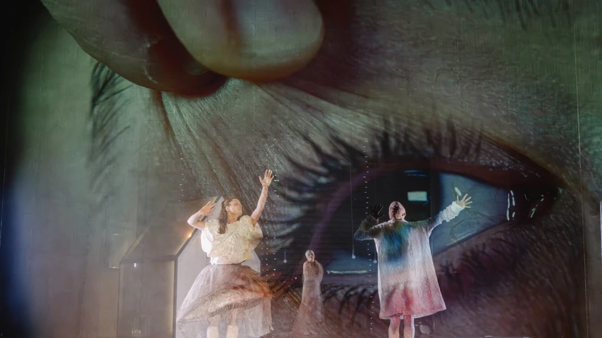 Menschen auf einer dunklen Bühne, dahinter Projektionen