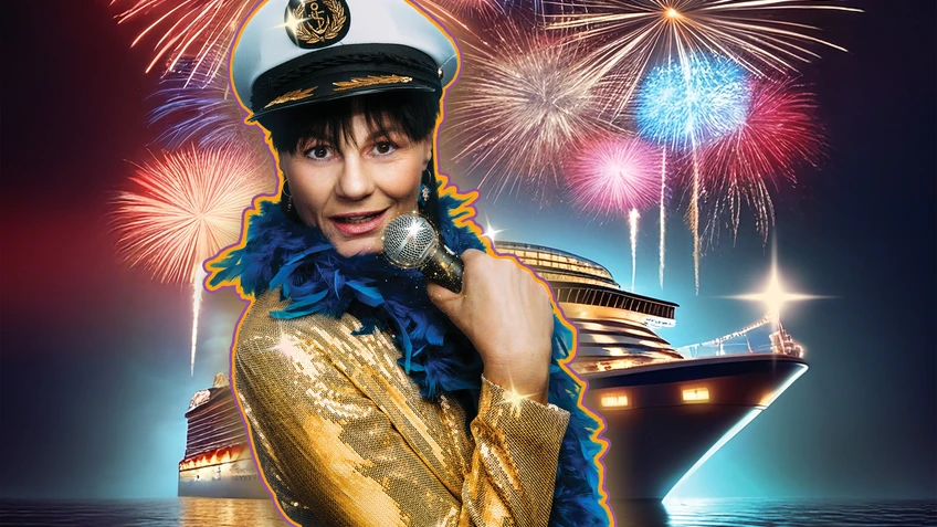 Eine Frau in glitzernder Kleidung mit einer Kapitänsmütze und Mikrophon vor einem großen Kreuzfahrtsschiff unter einem Feuerwerk