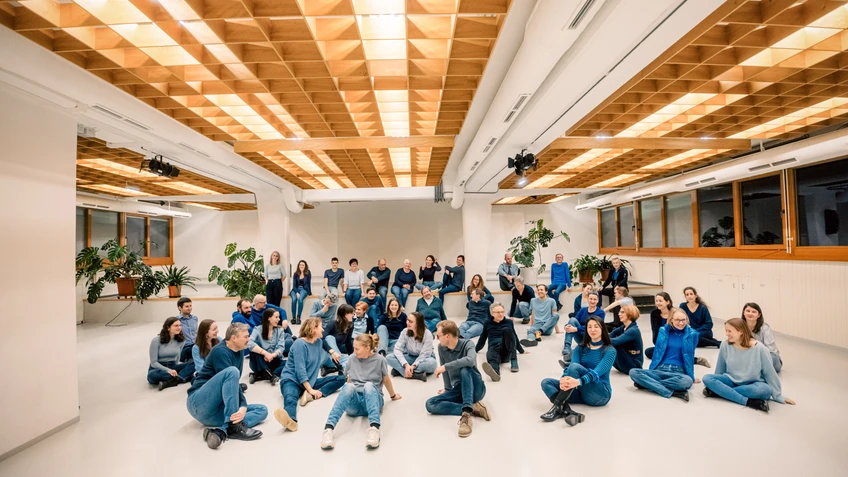 viele Menschen in einem großen Raum, alle tragen blaue Kleidung und sitzen in verschiedenen Positionen auf dem Boden