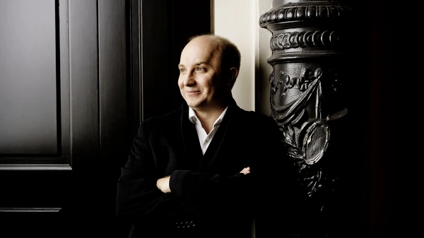 Mann in Anzug lehnt an einer prunkvollen dunklen Säule vor einem großen Tor 