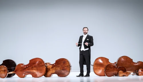 Fabien Gabel im Frack vor einem weißen Hintergrund, um ihn herum auf dem Boden stehen Orchesterinstrumente. 