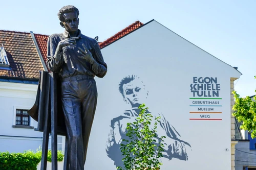 Statue des Künstlers Egon Schiele vor einem Gebäude mit großflächigem Wandbild und Schriftzug „Egon Schiele Tulln“.