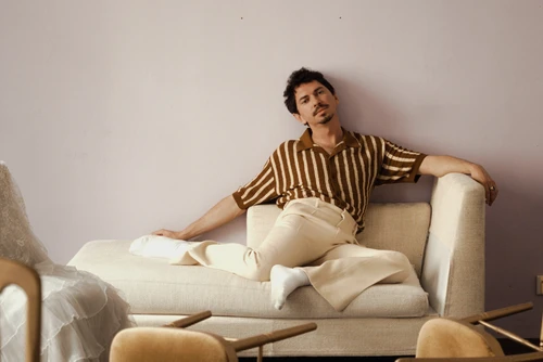 Julian Le Play sitzend auf einem hellen Sofa vor einer blassrosa Wand. 