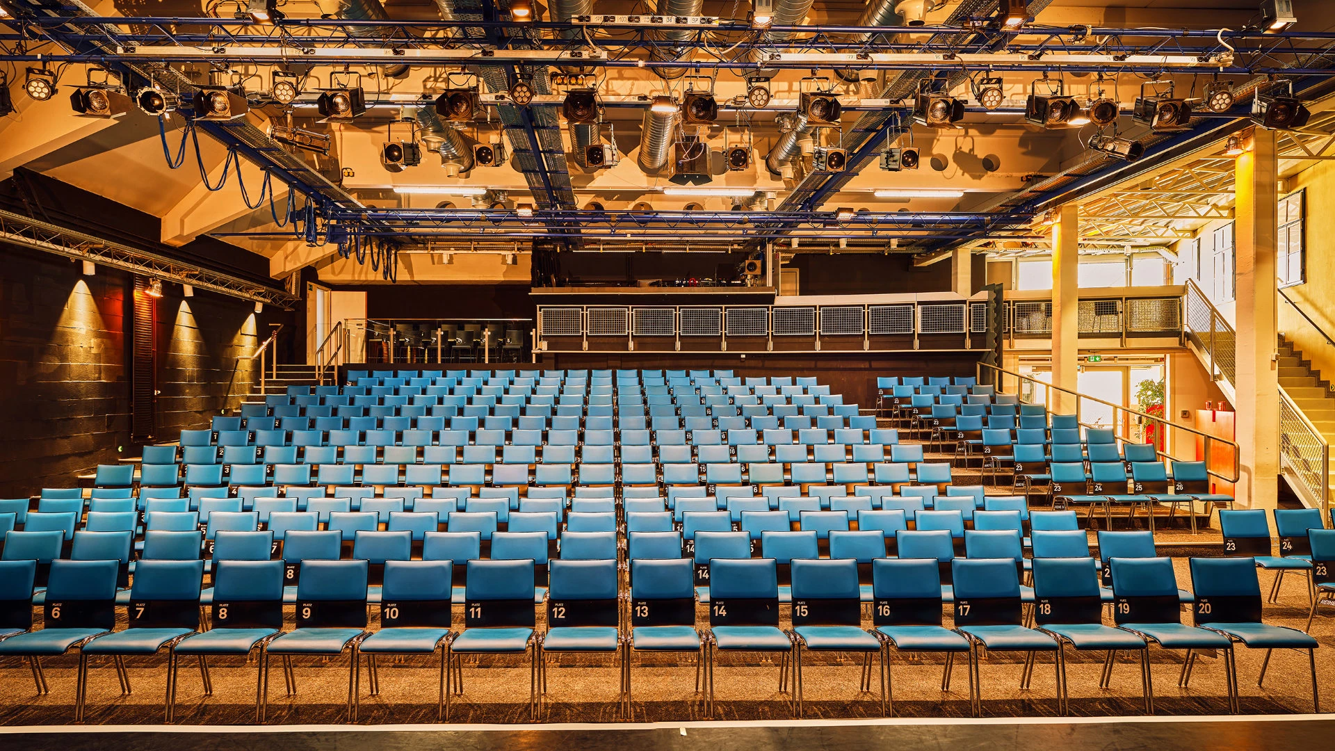 Innenansicht eines modernen Theatersaals mit nummerierten blauen Stühlen und ausgeklügelter Deckenbeleuchtung.
