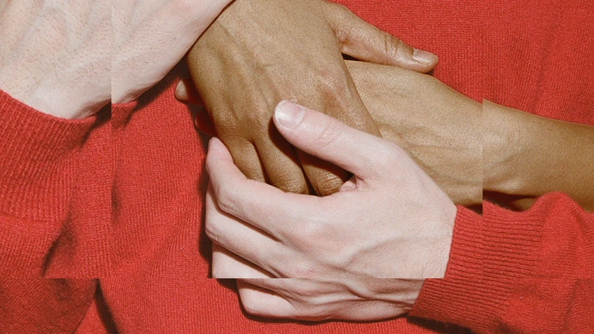 The theme for the Festspielhaus’s 2026/2027 season. The design features hands touching, a sleeve in a deep red colour against a red background created by the colour of the jumper.