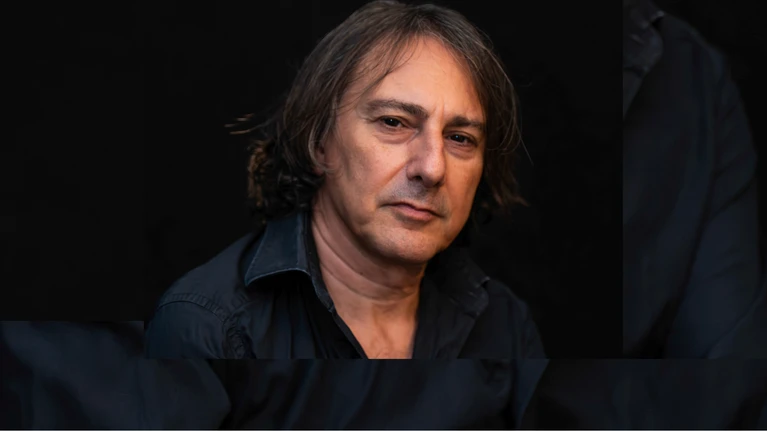 A portrait photograph of Pippo Pollina wearing a black shirt against a black background.