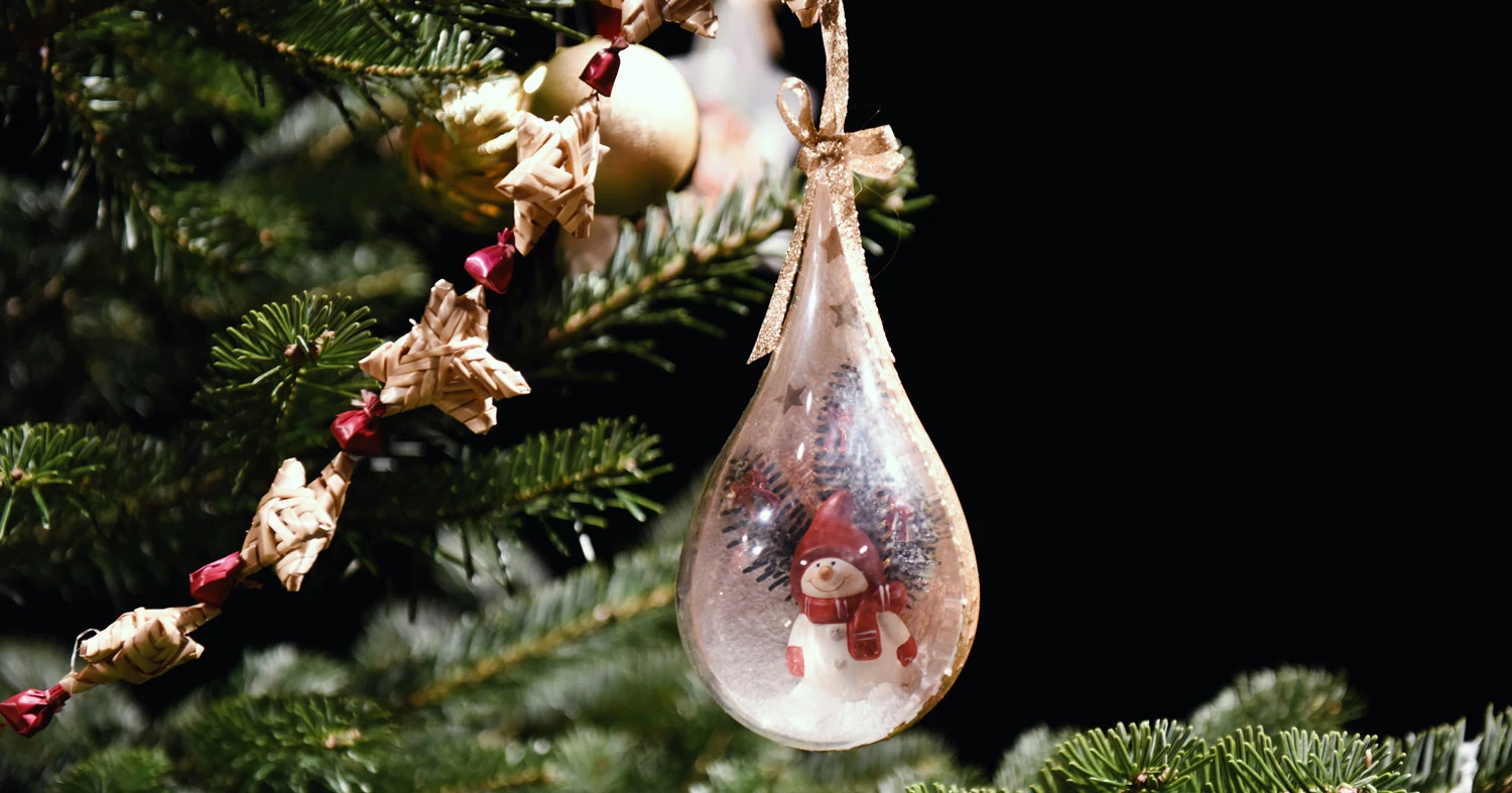 Tropfenförmige, transparente Chrsitbaumkugel mit Schneemann an Tannenbaumzweigen