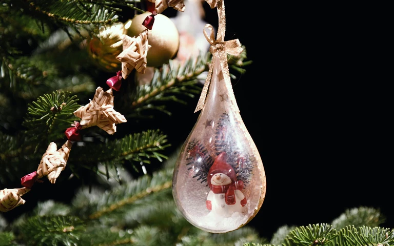 Tropfenförmige, transparente Chrsitbaumkugel mit Schneemann an Tannenbaumzweigen