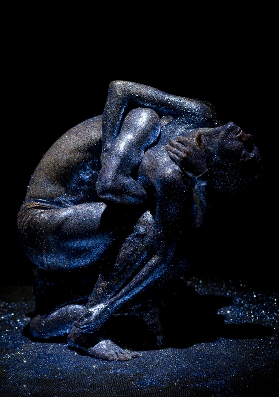 Szene aus ‚Mirage‘ mit zwei eng umschlungenen Tänzer:innen des Grand Théâtre de Genève, die in glitzernde Farbe gehüllt sind, umgeben von minimalistischer Kulisse, choreografiert von Damien Jalet und Kohei Nawa.