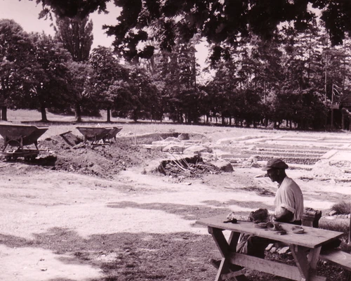 Grabung 1950 im Spaziergarten, Mann sitzt auf Bank vor den Ruinen 