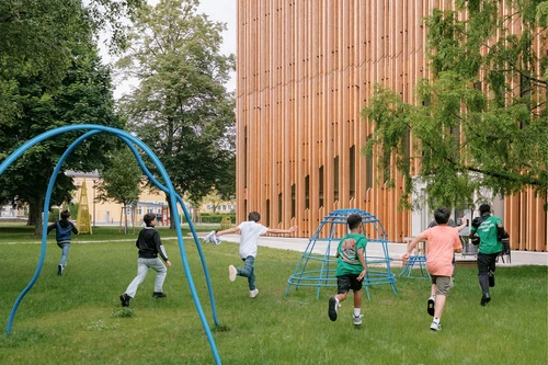 Kinder laufen über eine grüne Wiese auf den Holzbau des KinderKunstLabor zu.