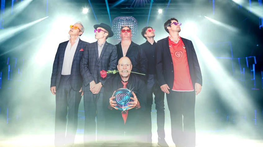 Eine Band bestehend aus sechs Männern in bunten herzförmigen Sonnenbrillen, einer trägt eine Rose im Mund