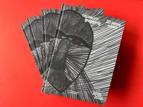 Auf einem roten Tisch liegen 4 exemplare eines Buchs wo drauf zu lesen ist "museum gugging, 20 jahre" residenz verlag. Am Cover ist eine Zeichnung eines Gesichts eines Löwen