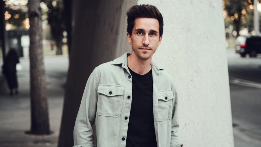 Mann in hellem Hemd und dunklen Haaren vor einem Betonpfeiler