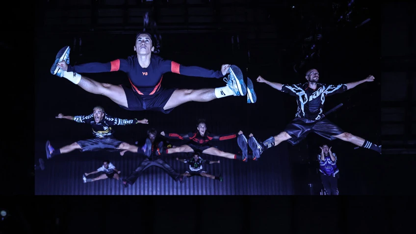 Performancefoto von "Trailer Park", choreografiert von Moritz Ostruschnjak, getanzt von tanz mainz. Die Tänzer:innen in oversized Sporttrikots springen synchron einen Split.