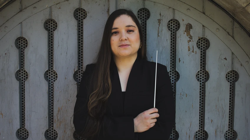 Junge Frau in dunkler Kleidung und langen Haaren mit Taktstock in der Hand