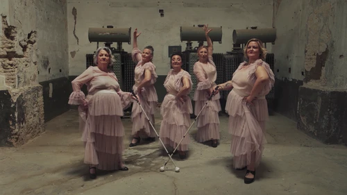 A still from the short film ‘In My Skin’ by Sándor M. Salas, showing five dancers in pale pink tulle dresses forming a dance formation – two dancers standing further forward in the frame are each holding a white cane, which they cross in the centre of the frame.