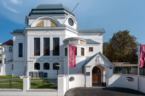 Frontansicht der renovierten Synagoge mit weißer Fassade, Rundbogenfenstern und hebräischer Inschrift.