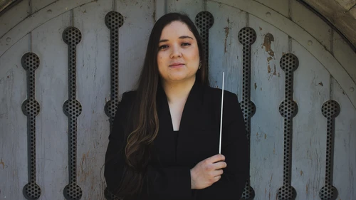 Junge Frau in dunkler Kleidung und langen Haaren mit Taktstock in der Hand