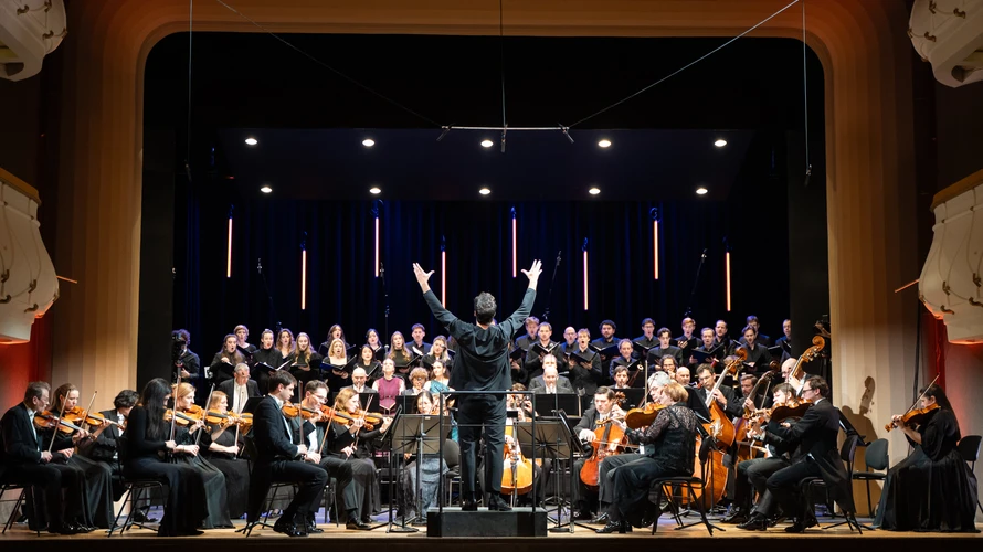 Orchester, Dirigent und Sänger musizieren auf einer Bühne