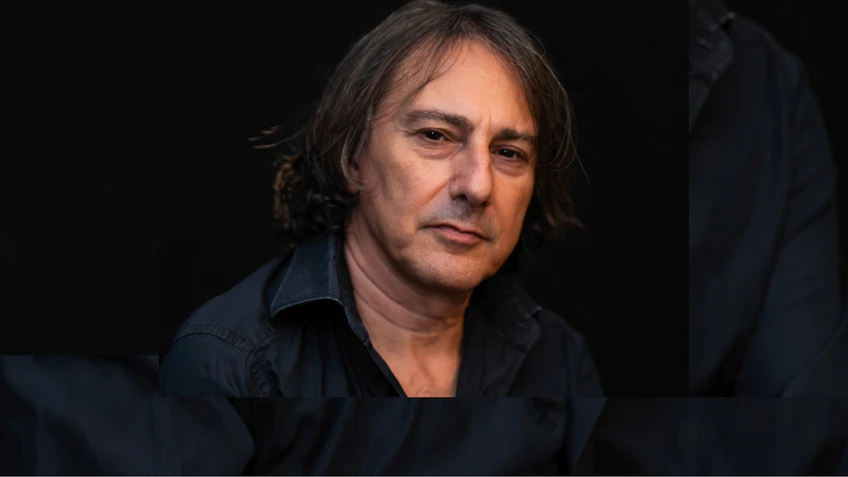 A portrait photograph of Pippo Pollina wearing a black shirt against a black background.