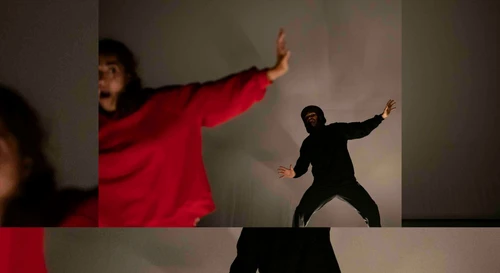 A performance photo from ‘Little Red Riding Hood’, choreographed by Sylvain Huc. The photo shows two dancers, one wearing a bright red tracksuit and the other a black tracksuit.