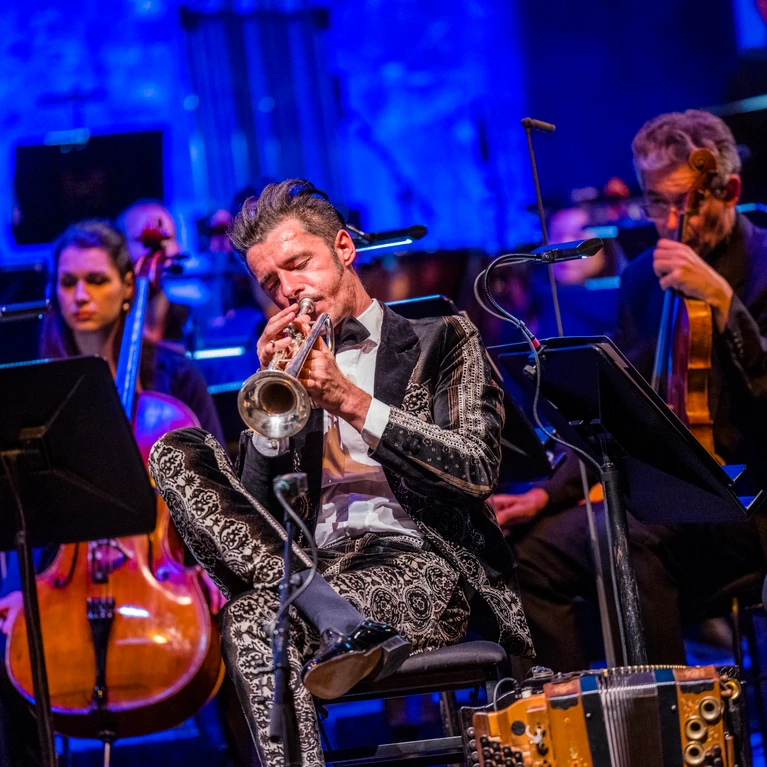 Herbert Pixner spielt mit dem Tonkünstler-Orchester auf einer großen Bühne, Musiker mit traditionellen und klassischen Instrumenten.