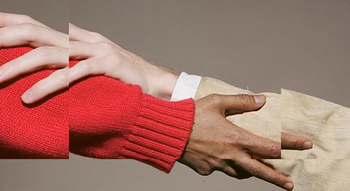 The theme for the Festspielhaus’s 2026/2027 season. The image shows hands touching, or rather two hands touching each other’s arms in a supportive gesture; one person’s sleeve is a deep red, the other’s a light beige, set against a dark beige background.