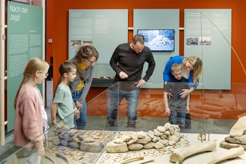 Familie betrachtet prähistorische Funde in einer Glasvitrine Infotafeln im Hintergrund