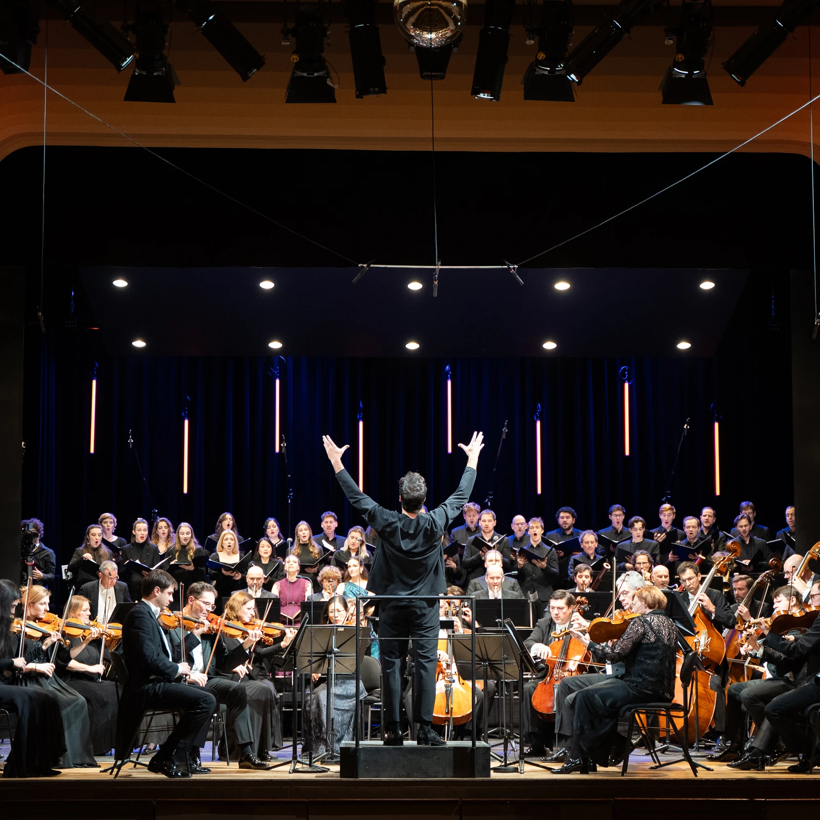 Orchester, Dirigent und Sänger musizieren auf einer Bühne