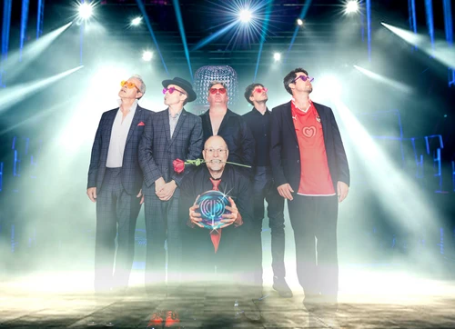 Eine Band bestehend aus sechs Männern in bunten herzförmigen Sonnenbrillen, einer trägt eine Rose im Mund