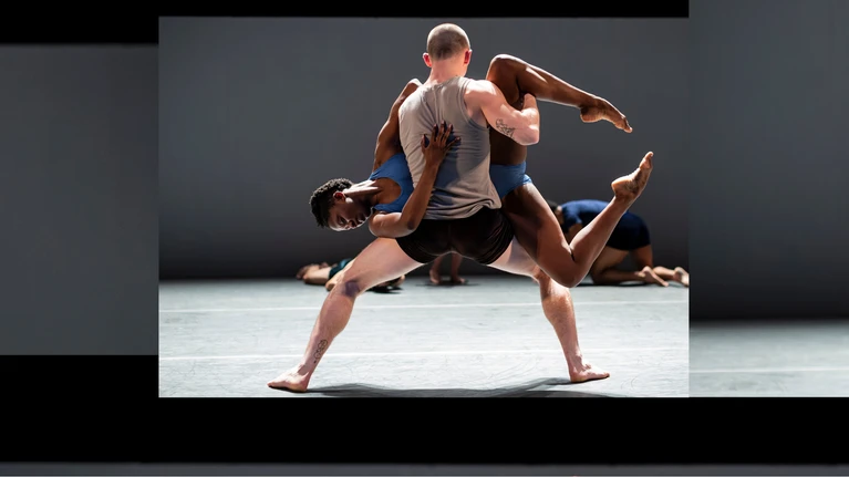 A performance photograph of ‘Sadeh21’, choreographed by Ohad Naharin. It shows two dancers from the Batsheva Dance Company – a male dancer lifting a female dancer sideways.