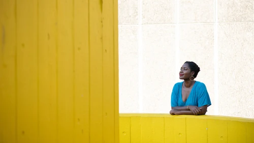 Frau in blauem Kleid im Hintergrund, im Vordergrund große gelbe Wände