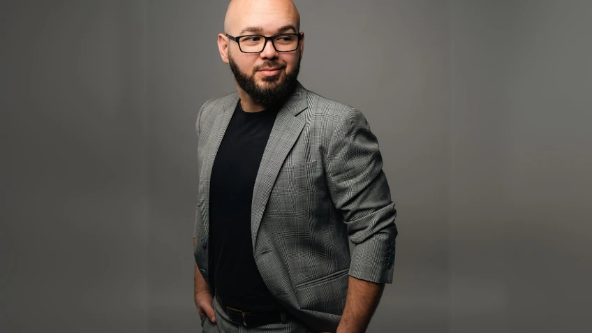 Mann mit Glatze, Bart und Brille in grauem Anzug vor grauem Hintergrund