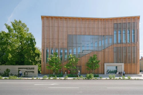 The wooden structure of the KinderKunstLabor from the outside with people passing by.