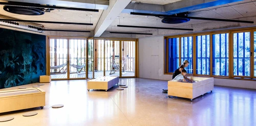 There are three interactive wooden tables in The One Lab at KinderKunstLabor. A boy and his mum are playing with sand at one of them.