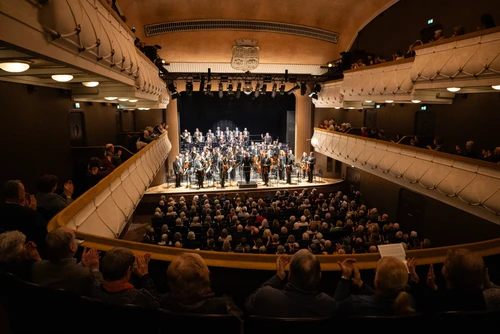 Voller Konzertsaal mit Orchester auf der Bühne