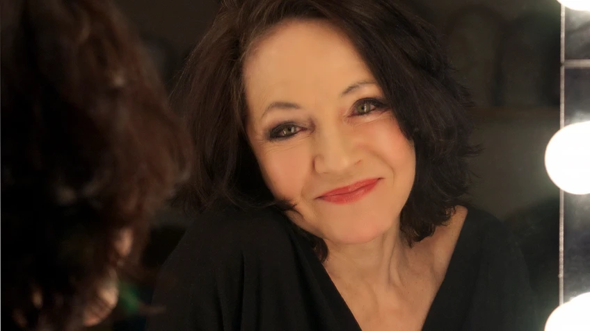 Maria Bill schaut aus dem Spiegel, dunkle Haare, roter Lippenstift