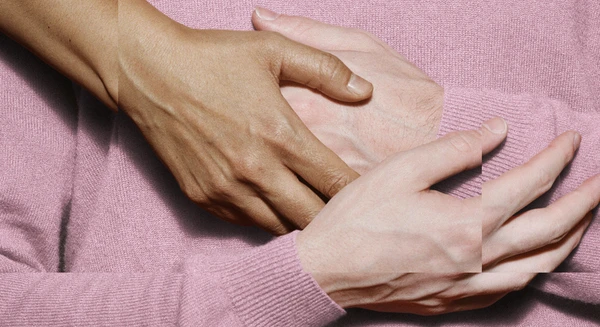 The theme for the Festspielhaus’s 2026/2027 season. The image shows hands touching against a pink background, which derives from the colour of the jumper worn by a person whose arms are crossed in front of their torso.